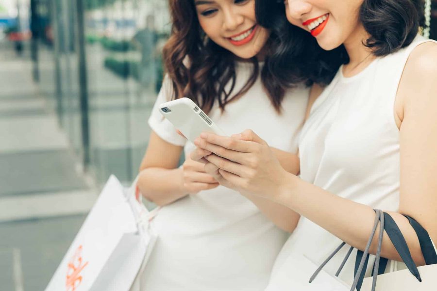 Beautiful asian girls with shopping bags using smartphone at the mall