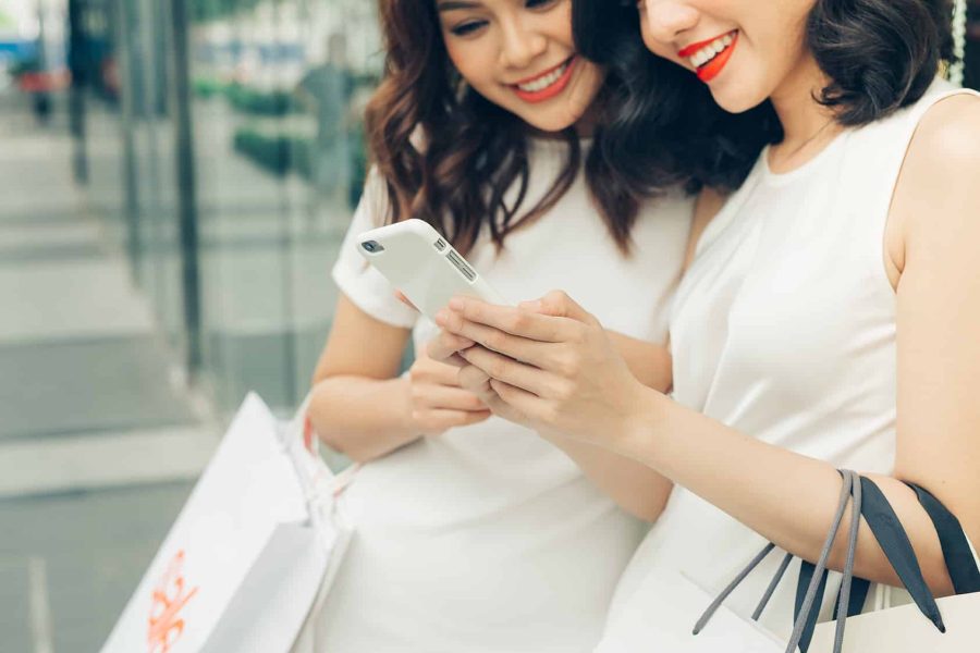 Beautiful asian girls with shopping bags using smartphone at the mall